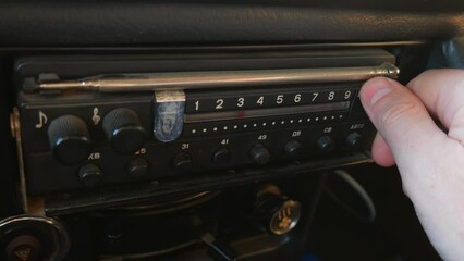 The old radio is tuned by turning the dial in the car. The radio dials the number, looks for stations. Old radio of the USSR. Human hand