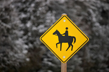 Yellow Caution Horse Riding Sign in a Rural Setting in Winter Isolated against a Snowy Forest