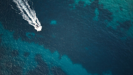 Aerial top view of the teal clear water of the ocean with a white boat
