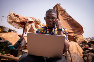 Young African boy works with his laptop and makes a phone call, he is at the market