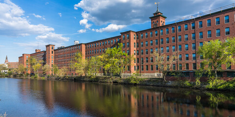 Historical building of a cotton factory with a clock tower in an old industrial park  on Nashua River in May. Nashua, New Hampshire, USA