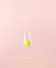 Yellow tennis ball in a transparent drinking glass on a pink background. Minimal concept.