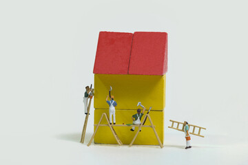a team of painters with wooden ladder and scaffolding is painting a yellow house with a red roof