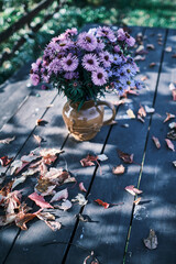 Autumn purple floral bouquet in a vase on a garden table covvered with leaves