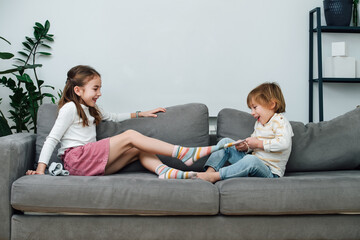 Boy pulling off sock of a girl, they are preparing for a tickling competition - obrazy, fototapety, plakaty