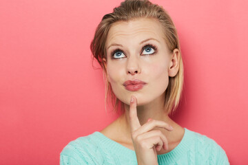 Fototapeta premium Hard choice. A beautiful young woman thinking to herself while isolated on pink.