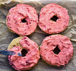 pink strawberry cream cheese spread onto sliced seeded bagel halves for bagel sandwiches