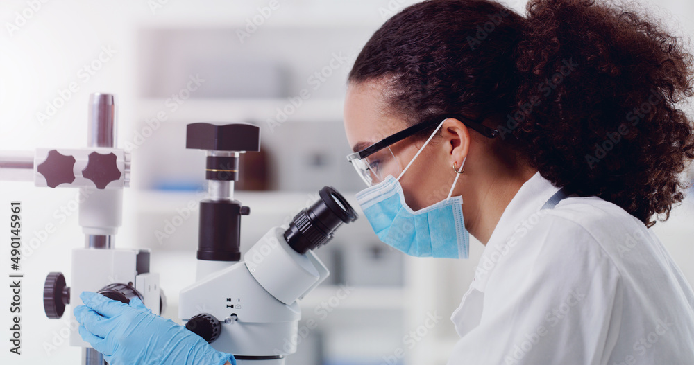 Wall mural the solution must be here somewhere. shot of a young scientist using a microscope in a lab.