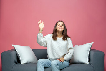 Smiling beautiful young girl waving hand, greeting with audience or subscribers, sitting on sofa....