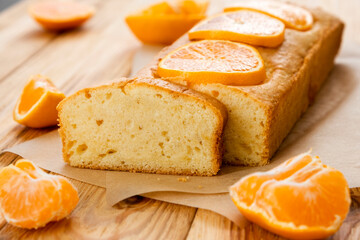 Loaf of delicious tangerine pound cake on parchment with pieces of mandarin on rustic wooden...