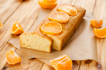Moist orange fruit pound cake on parchment on rustic wooden background with slices of orange. Delicious breakfast, traditional English tea time. Reciepe of orange pie loaf.