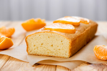 Moist orange fruit pound cake on parchment on rustic wooden background with slices of orange. Delicious breakfast, traditional English tea time. Reciepe of orange pie loaf. - obrazy, fototapety, plakaty