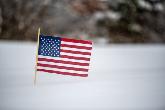 Closeup of a small US flag in the snow in a field with a blurry background