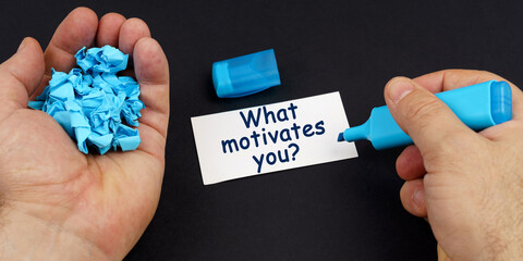 In the hands of crumpled paper, a marker, next to a business card with the inscription - What motivates you