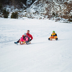Family sledding on the snow and having fun in winter.