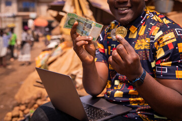 Close-up of the hands of an African boy holding a Bitcoin and Ethereum coin and a 5000 CFA franc...