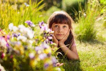 Happy little girl laying on a grass in the garden.