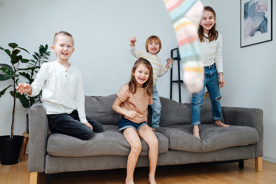 Mischievous children throwing socks at the camera, jumping on a couch.