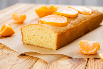 Moist mandarin pound cake on parchment with pieces of fresh tangerine on rustic wooden background. Delicious breakfast, traditional tea time treat. Reciepe of American lemon pie loaf.