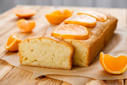 Loaf of gluten free tangerine cake with pieces of mandarin on rustic wooden background. Close up slice of citrus pie by classic recipe. Healthy nutrition, homemade vegan dessert.