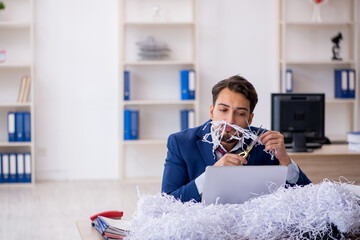Young male employee and a lot of cut papers in the office