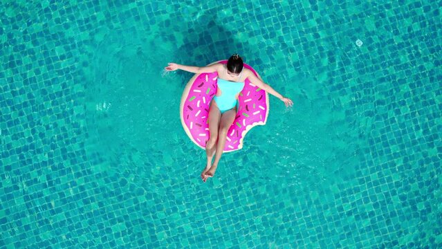 Top view of young asian woman in swimsuit on the pink donut lilo in the swimming pool.