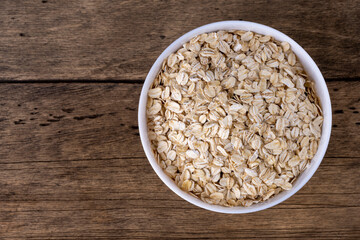 Dry rolled oatmeal in bowl on wooden background. Top view.