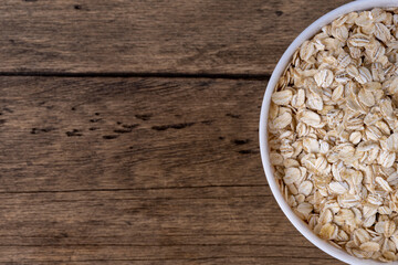 Dry rolled oatmeal in bowl on wooden background. Top view.