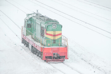Green shunting diesel locomotive on the railway tracks during a heavy snowstorm