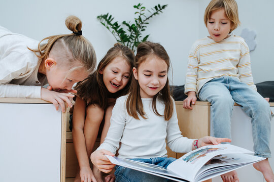 Entertained children gathered in a room to read book, all looking at it