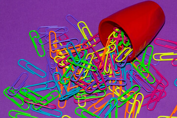 spilled colorful staples from a red cup on a pruple background