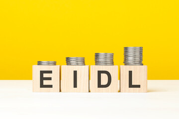 wooden cube on a concrete surface with text EIDL. copy space on right for design, yellow background