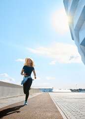 Young woman with fit body running on a sunny day. Female model in sportswear exercising outdoors. Female runner in black sportive clothes doing fitness