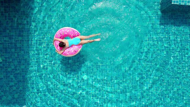 Top view of young asian woman in swimsuit on the pink donut lilo in the swimming pool.