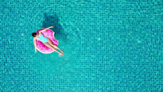Top view of young asian woman in swimsuit on the pink donut lilo in the swimming pool.