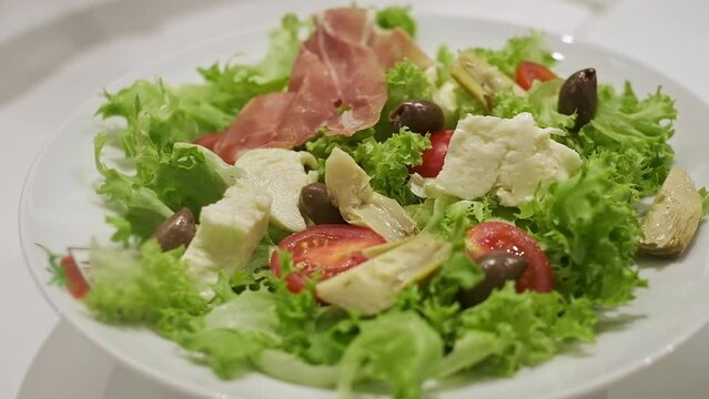 Appetizing Salad On Plate. It Consists Of Cheese Olives Meat Salad Leaves Meat. Cook Puts Salad Ingredients On Plate.