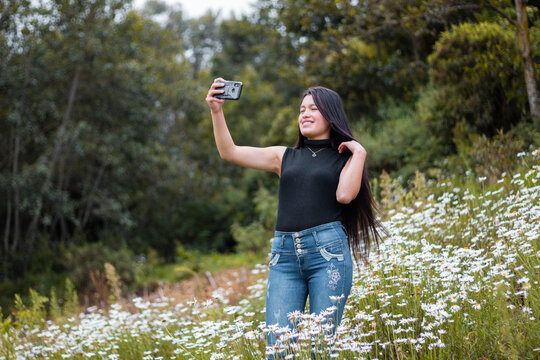 Joven atractiva sonriente  parado tom&aacute;ndose selfie  con su celular en las manos, tel&eacute;fono celular, naturaleza,