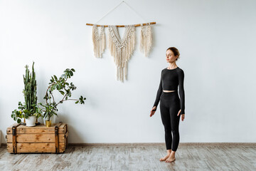 Yoga practice Tadasana mountain pose. A girl stands in Samasthiti performing an asana to relax the body. Black fitness clothes. © Aleksey