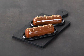Dessert without baking. Chocolate walnut cake in the form of a cylindrical bar, with mirror glaze on a serving board. Dark gray background