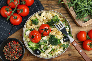 Bowl of delicious pasta with tomatoes, broccoli and cheese on wooden table, flat lay