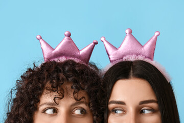 Young sisters with toy crowns looking at each other on color background, closeup