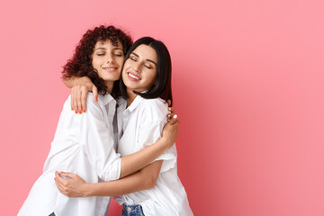 Happy sisters with closed eyes hugging on color background