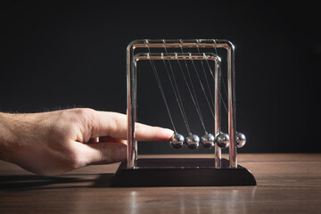 Male hand showing Newton's cradle balls on the wooden table. Business