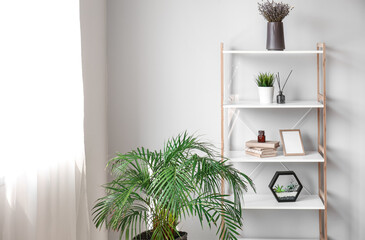 Shelving unit with decor and houseplants near light wall