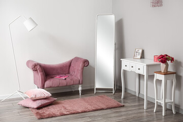 Interior of stylish room with pink armchair, mirror and tables