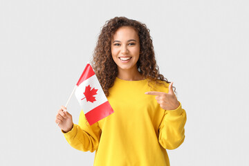 Beautiful young African-American woman with Canadian flag on light background