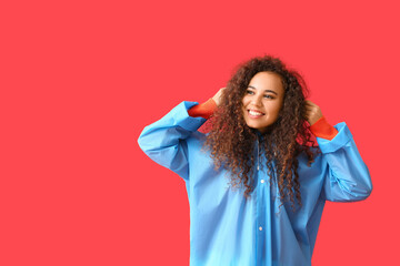 Young African-American woman in blue raincoat on red background