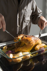 Unrecognizable man preparing a juicy oven baked chicken with vegetables.