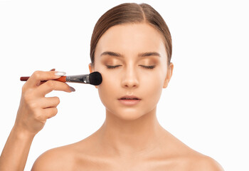 Portrait of a beautiful brunette girl with beautiful fresh makeup and healthy clean skin.Makeup artist holds a powder brush in her hands. Professional makeup concept