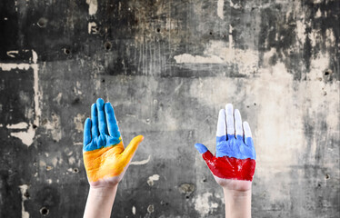 Hands painted in the colors of the flags of Russia and Ukraine are raised up against the background...